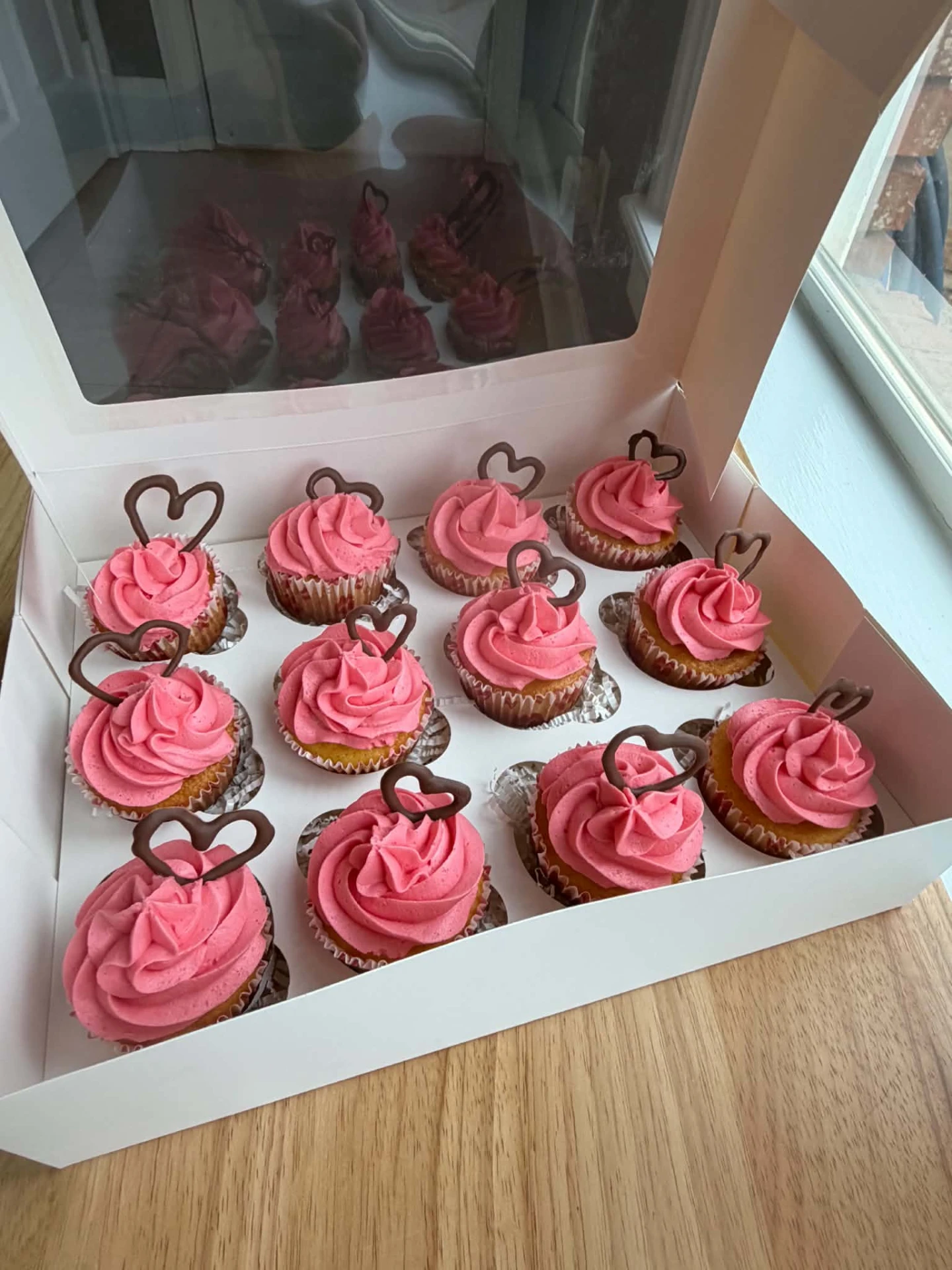 A dozen pink frosted cupcakes with chocolate hearts